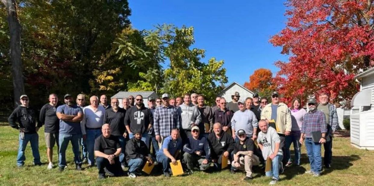 A group of predominantly male students posing together for a class photo in a backyard.