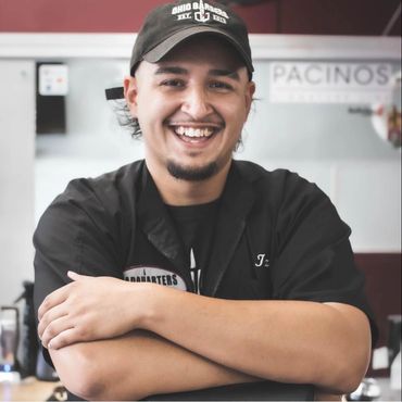 Smiling barber wearing a black cap and jacket in a barbershop.