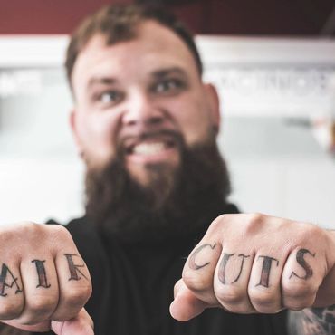 Man with tattooed knuckles spelling 'HAIR CUTS' shows fists.
