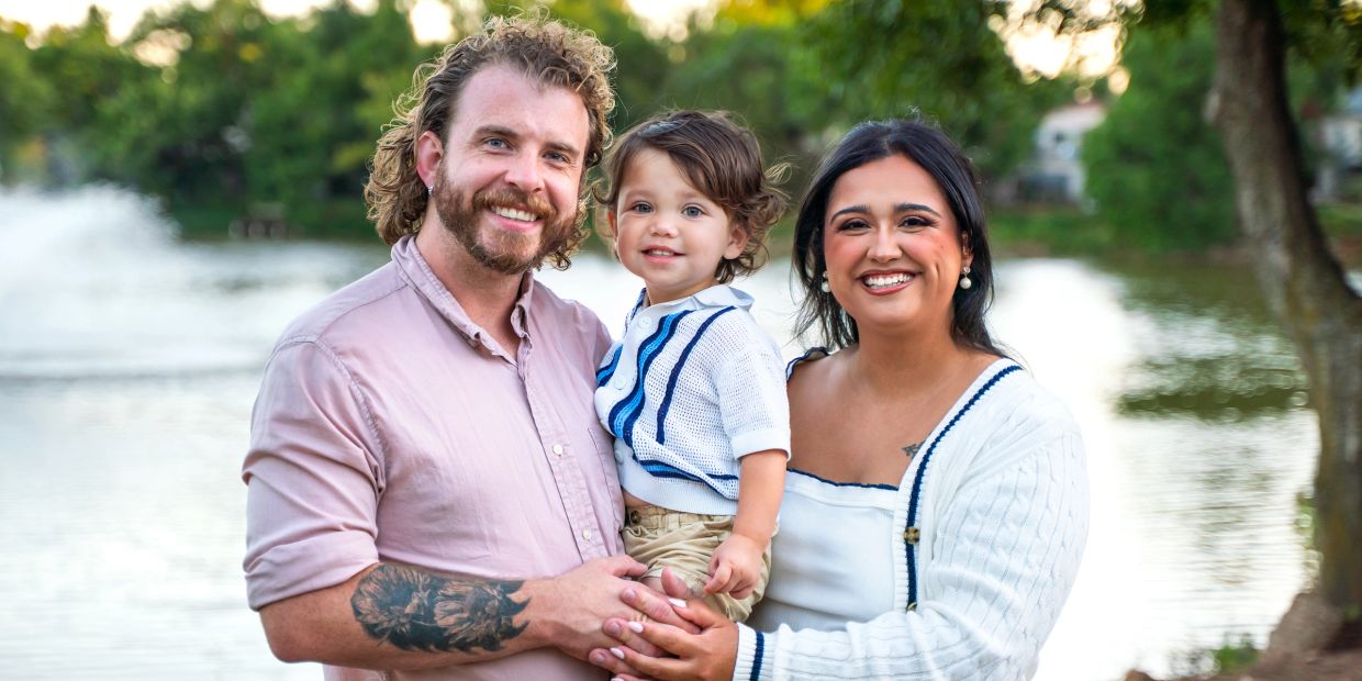 Happy family of three posing outdoors near a lake with smiles.