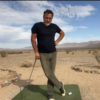 Man posing with golf club in desert area.