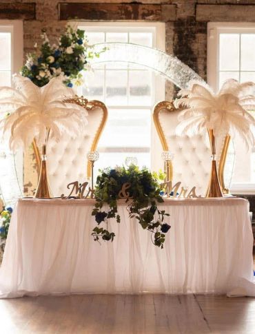Elegant wedding sweetheart table with tufted chairs and feather centerpieces.