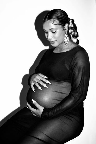 Pregnant woman gently holding her belly, captured in a black and white portrait.