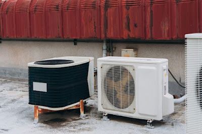 Two air conditioning units placed on a rooftop against a red wall.