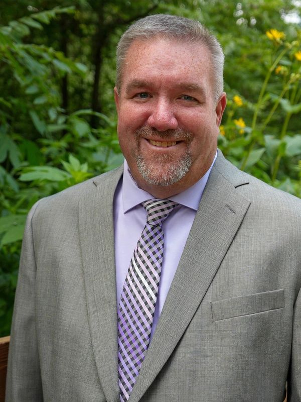Man in a gray suit smiling outdoors.
