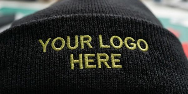 Black knit hat with yellow embroidered text 'YOUR LOGO HERE'.