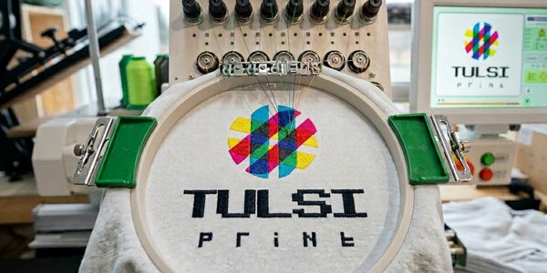 Embroidery machine stitching colorful Tulsi Print logo on fabric.