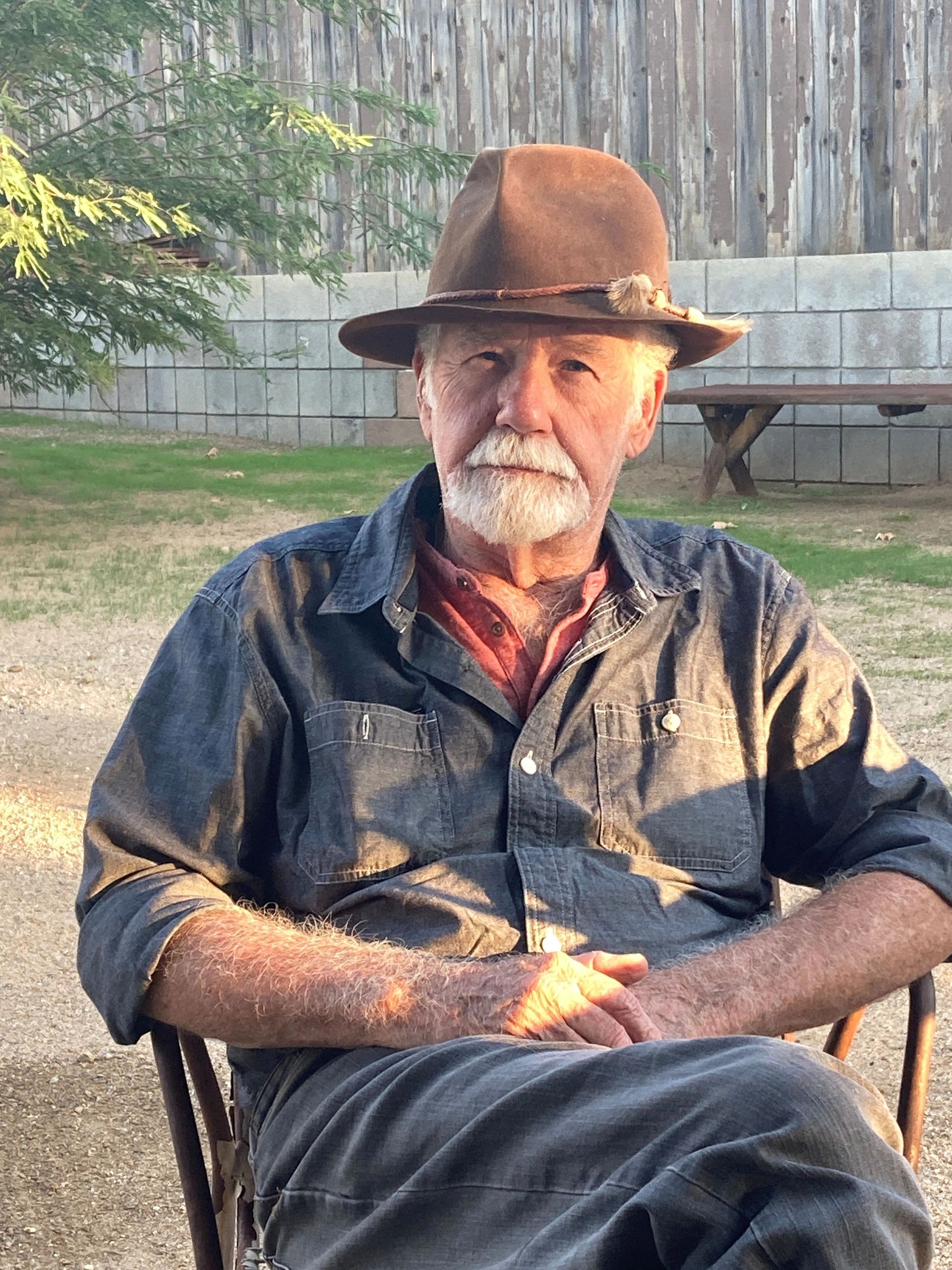 Elderly man with a hat sitting outdoors in natural light.