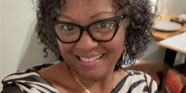Smiling woman with curly hair and glasses wearing a striped top.