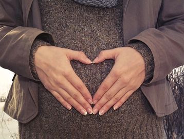 Heart-shaped-hand-over-pregnancy-bump-in-winter-clothes
