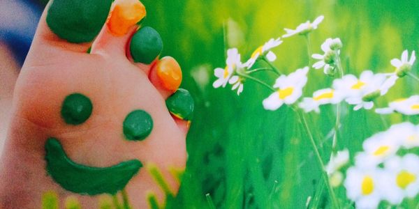 Painted-feet-with-a-smiley-face-in-a-field-of-daiseys-with-reflexology-written-above