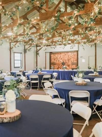 Image of Lodge-style Event Center with navy tablecloths and white chairs. Large barn doors in the ba