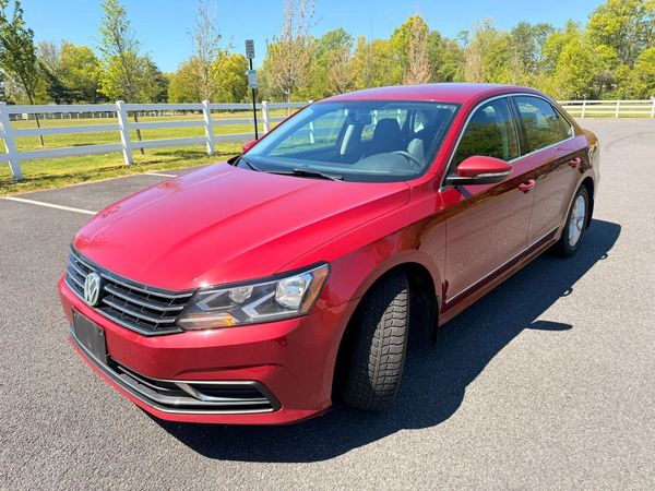 Red Volkswagen sedan parked on a sunny day near white fencing.