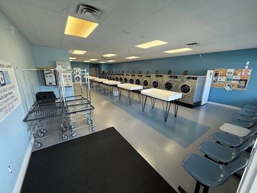 Clean, well-lit laundromat with washing machines, folding tables, and seating.