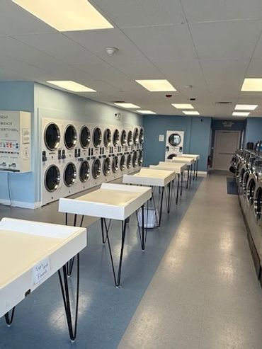 Interior of a clean laundromat with washers, dryers, and folding tables.