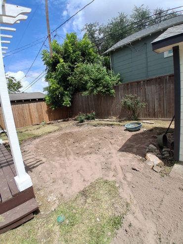 Backyard with freshly tilled soil, some plants, and a wooden fence.