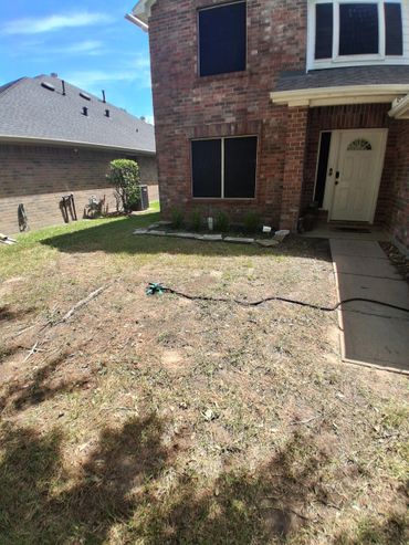 Dry lawn in front of a brick house with a sprinkler and shaded walkway.