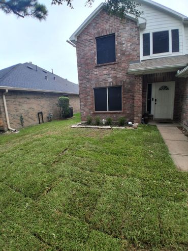 Newly laid sod in front yard of a brick house with blacked-out windows.