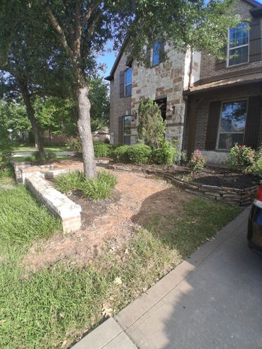 Front yard of a brick and stone house with a large tree and garden beds.