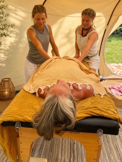 Two therapists giving a massage to a woman lying on a table outdoors.