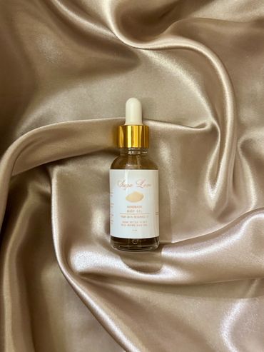 A bottle of Suga Love handmade body oil on silky fabric.