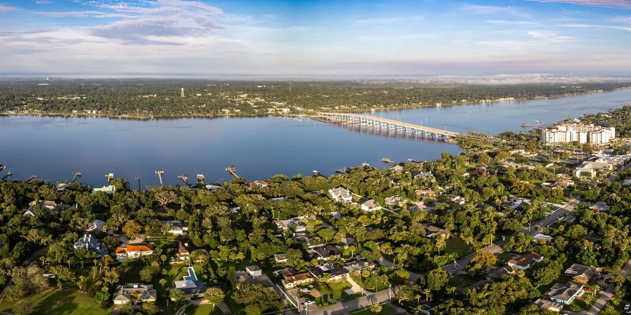 A sprawling riverside cityscape with a long bridge and abundant greenery.