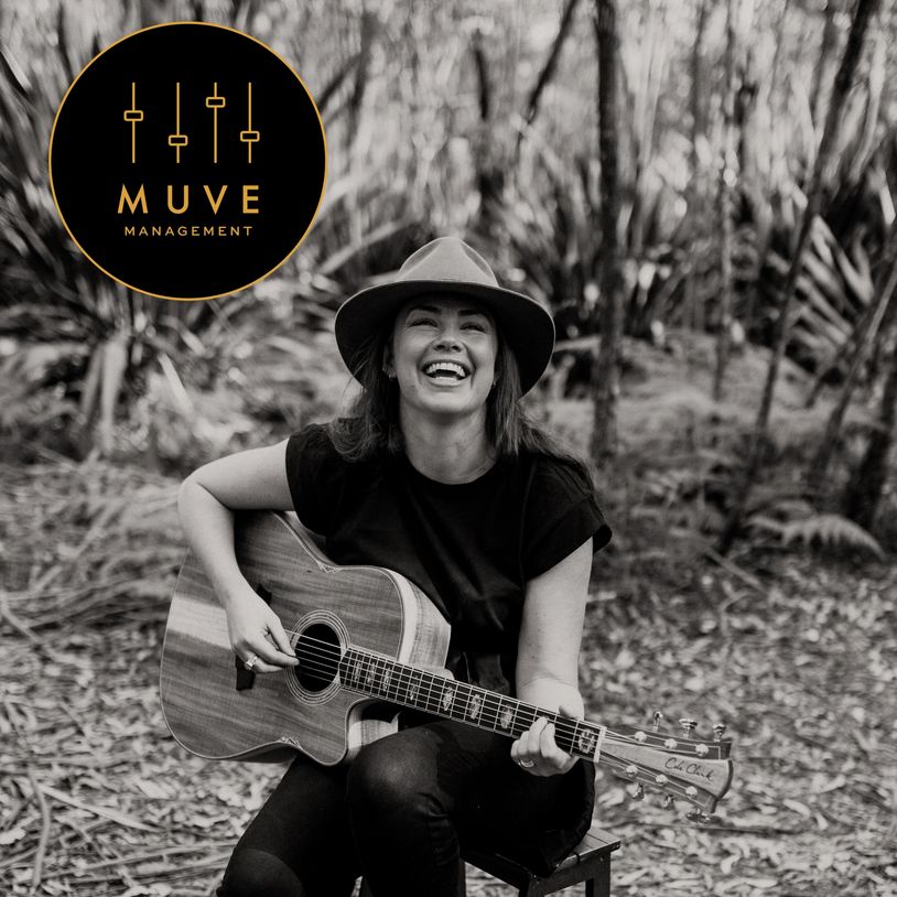 Woman joyfully playing guitar outdoors, with MUVE Management logo.