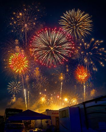 Colorful fireworks light up the night sky above a campsite.