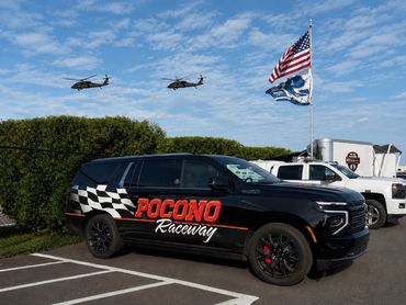 Black SUV with Pocono Raceway branding parked with helicopters and flags in background.