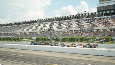 Stock cars racing on a track with spectators in the stands.