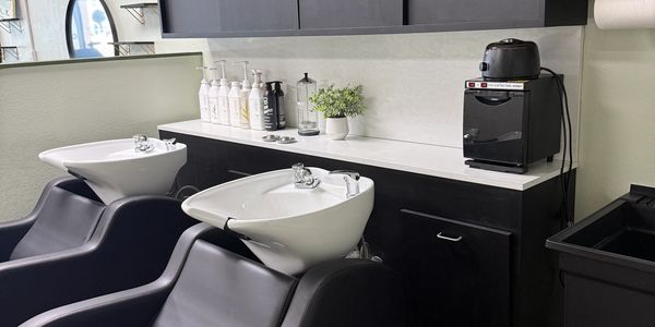 Modern salon shampoo station with black chairs and white sinks.