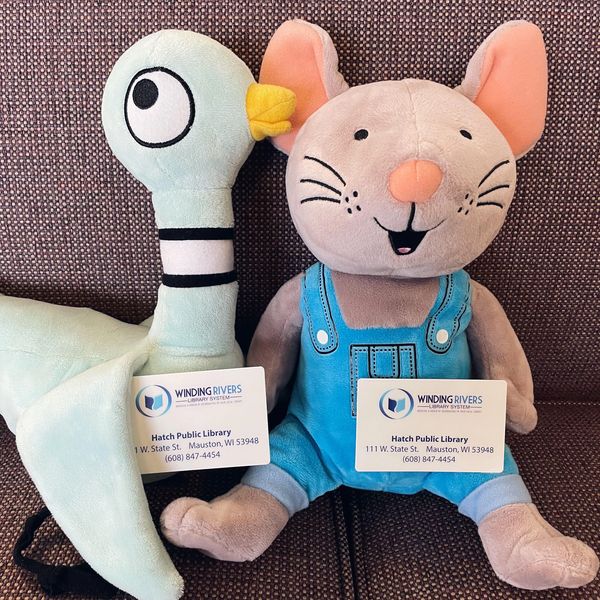 Two book character stuffed animals sitting on a couch holding Hatch Public Library library cards