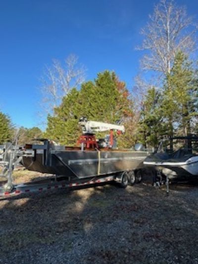 A boat on a trailer parked outdoors with trees and a clear blue sky.