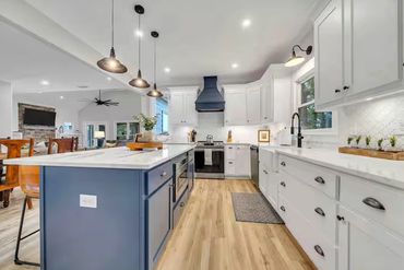 Modern kitchen with white cabinets, blue island, and wooden floors.