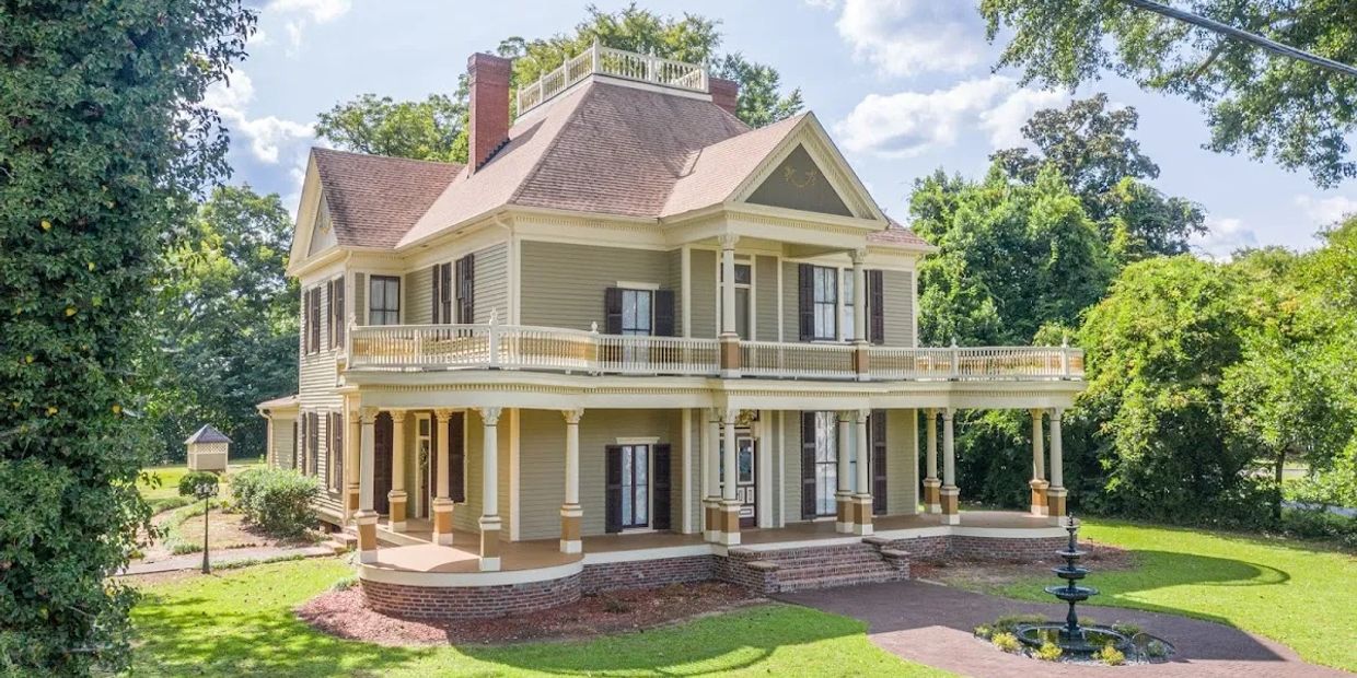 Elegant two-story historic house with wraparound porch and lush greenery.