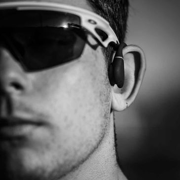 Close-up of a man wearing sunglasses and wireless earphones.