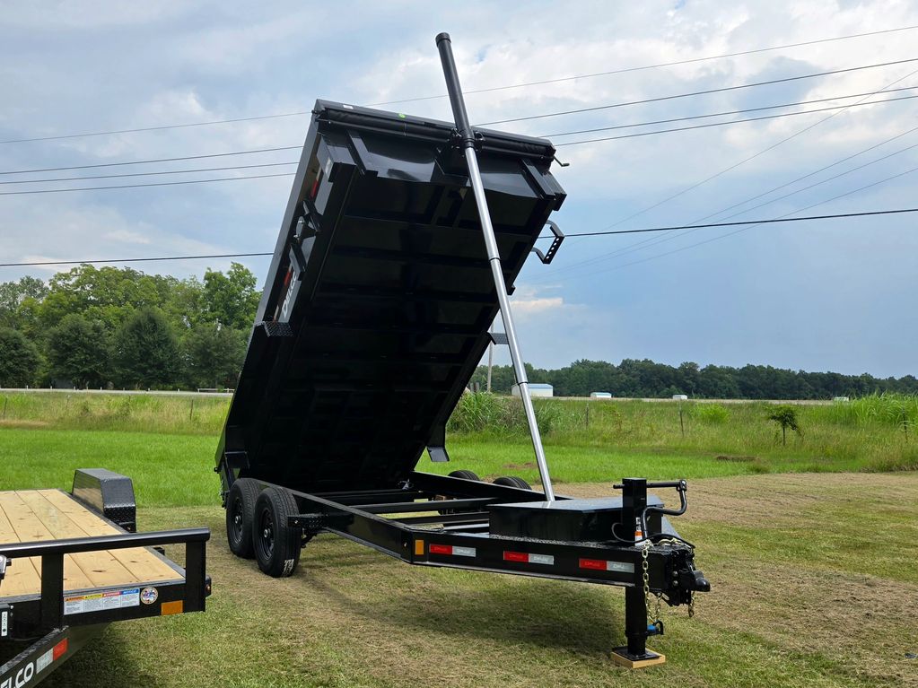Black dump trailer with raised bed on grassy field under cloudy sky.