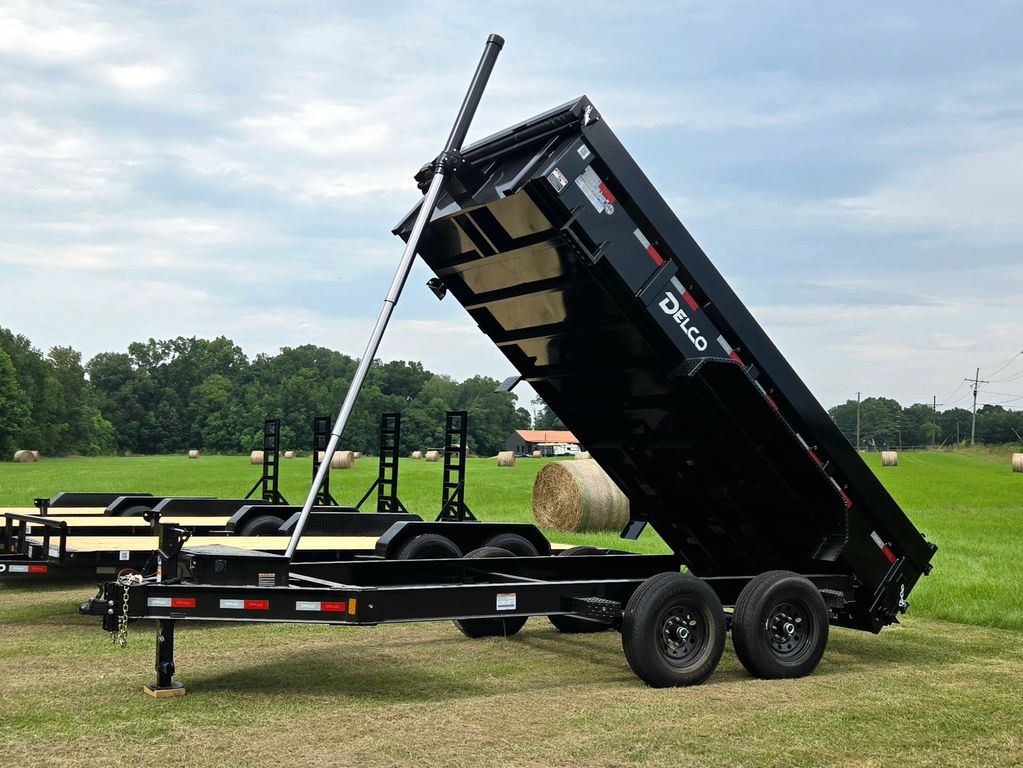 Black dump trailer with raised bed parked on grassy field under cloudy sky.