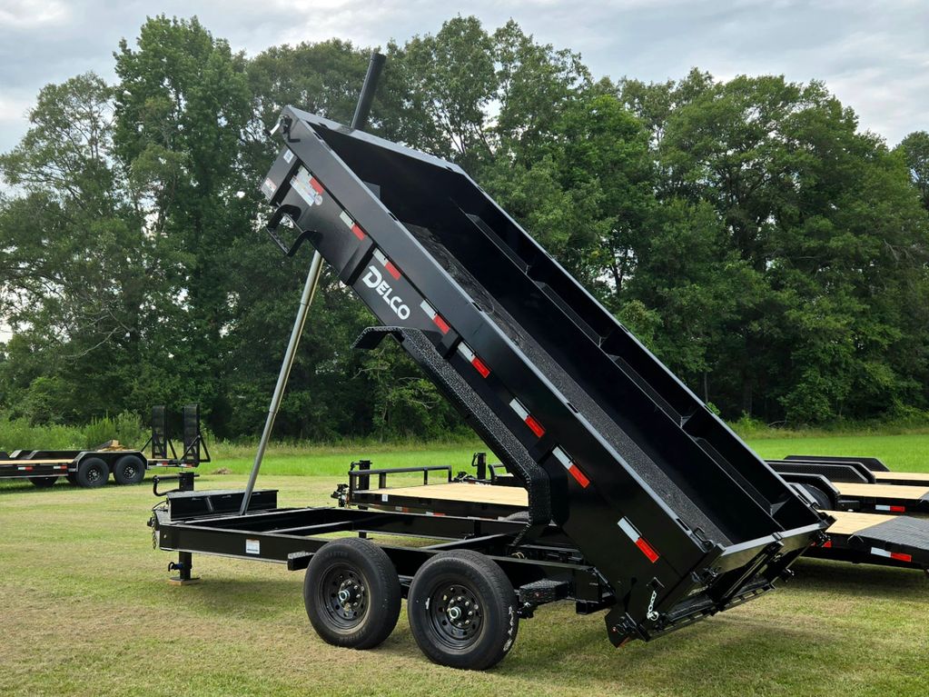 Black Delco dump trailer with raised bed on grassy field.