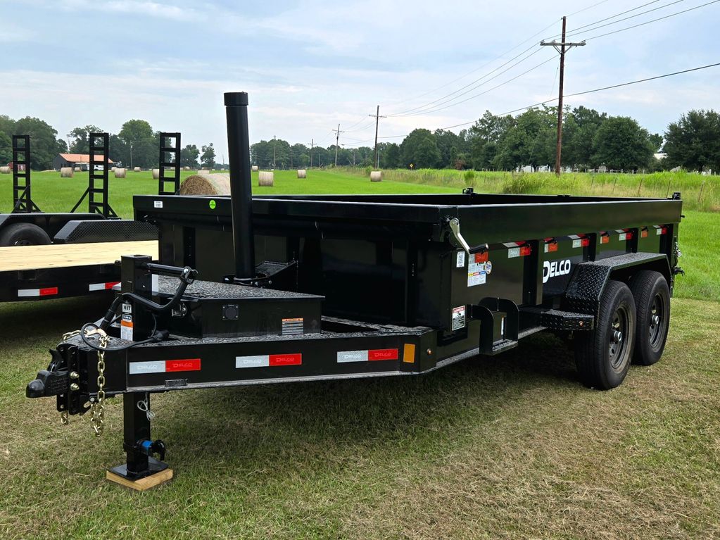 Black Delco dump trailer parked on grass near a field with hay bales.