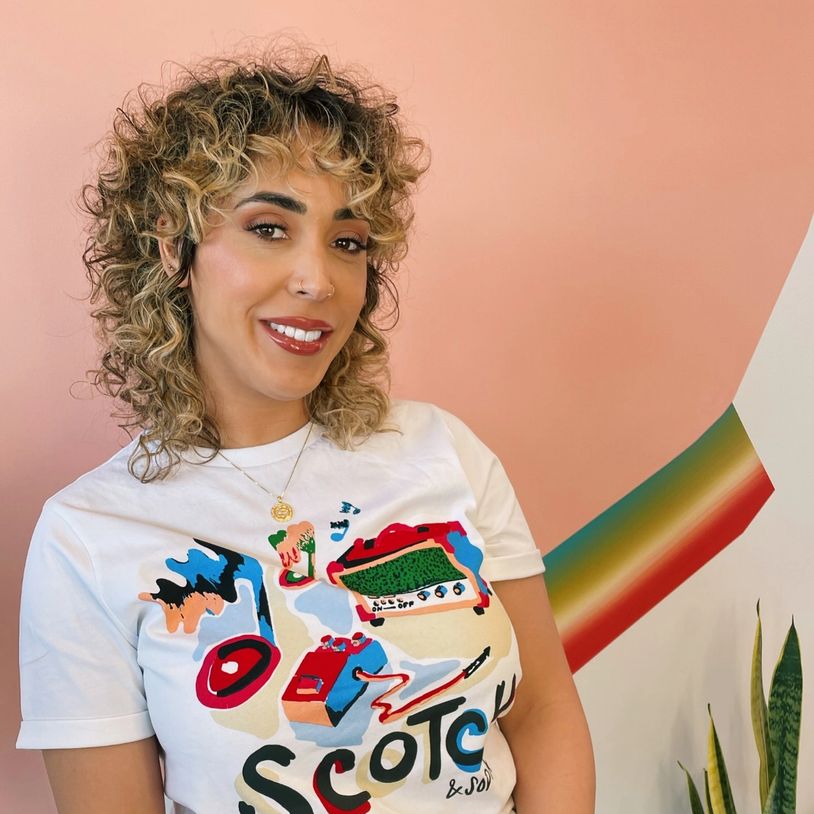 Smiling woman with curly hair and colorful t-shirt against peach wall.