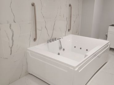 Modern white bathtub with marble tiles and stainless steel handles.