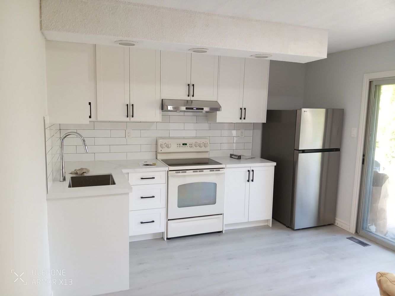 Modern kitchen with white cabinets, stainless steel fridge, and light gray flooring.