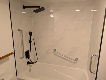 Modern bathtub and shower with sleek black fixtures and grab bars.