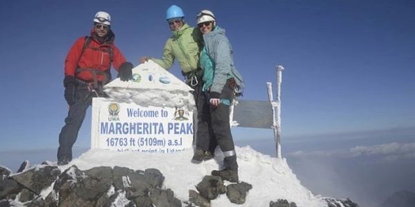 Three climbers at the summit of Margherita Peak with a sign indicating the altitude.