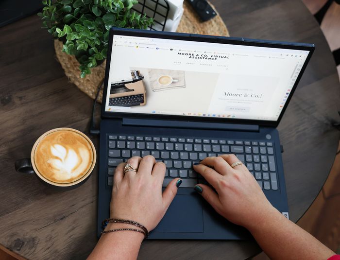Person typing on a laptop with coffee and plant nearby.
