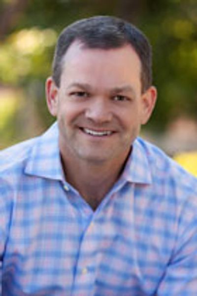 Smiling man in a blue checkered shirt outdoors.