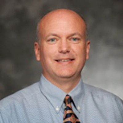 Professional headshot of a middle-aged man in a shirt and tie.