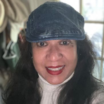 Woman smiling, wearing a blue cap and white turtleneck.