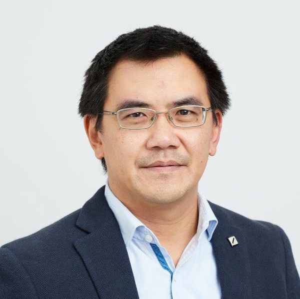 Man wearing glasses and a navy blazer, smiling slightly.